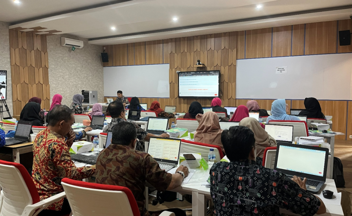 Suasana pelatihan di dalam ruang kelas modern di mana puluhan peserta sedang duduk menghadap laptop masing-masing sambil memperhatikan layar presentasi di depan kelas.