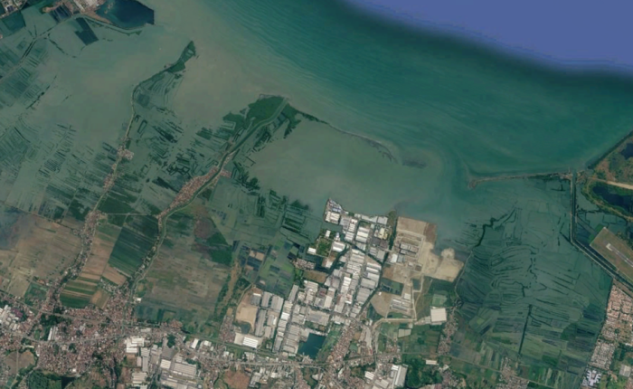 Citra satelit wilayah pesisir yang menampilkan perairan laut berwarna hijau kebiruan, batas garis pantai, serta daratan yang didominasi oleh area tambak, pemukiman, dan kawasan industri.