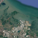 Satellite imagery of a coastal area showing blue-green ocean waters, the coastline boundary, and a landmass dominated by aquaculture ponds, settlements, and industrial zones.