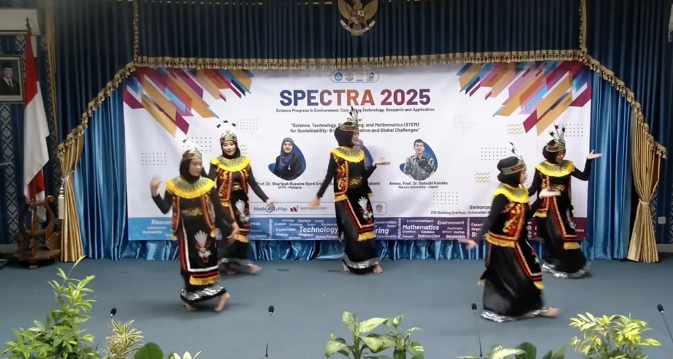 Five female students wearing traditional black dance costumes with gold accents and headpieces performing on a stage with a SPECTRA 2025 event banner in the background.