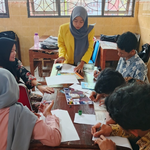 Five students, two males and three females, wearing yellow alma mater jackets, stand in a row in front of a building labeled UNNES Library. They are holding the Fortpoli game board, a deck of challenge cards, and a laptop displaying the digital design of the medium.