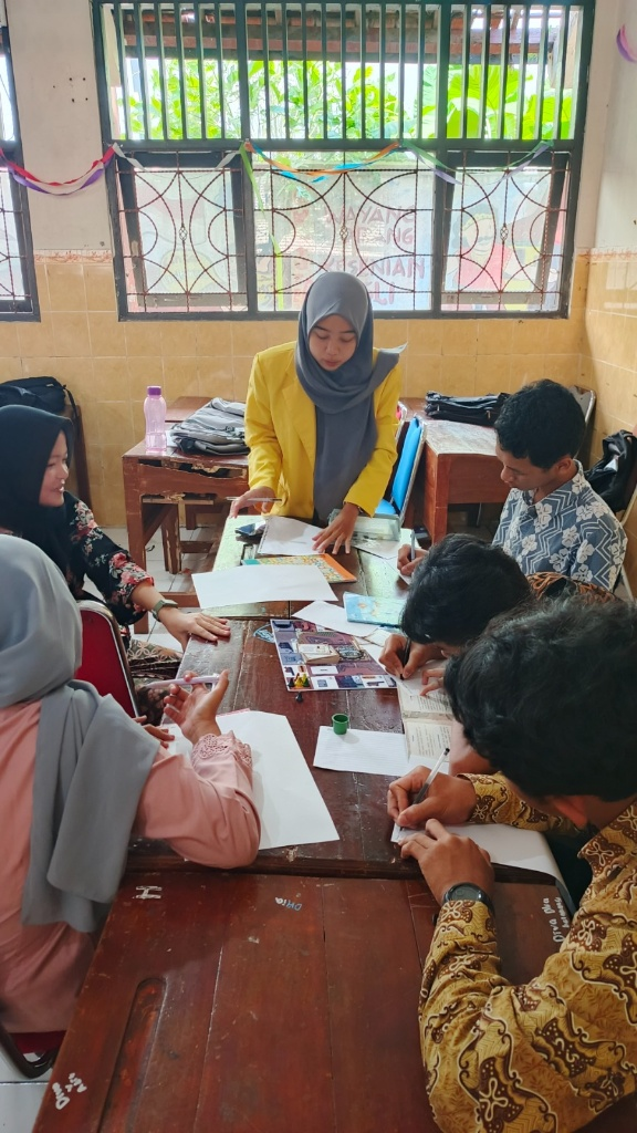 Five students, two males and three females, wearing yellow alma mater jackets, stand in a row in front of a building labeled UNNES Library. They are holding the Fortpoli game board, a deck of challenge cards, and a laptop displaying the digital design of the medium.
