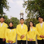 Lima mahasiswa yang terdiri dari tiga laki-laki dan dua perempuan mengenakan jas almamater kuning khas UNNES, berdiri sejajar menghadap kamera di luar ruangan dengan latar belakang pepohonan dan tugu konservasi kampus.