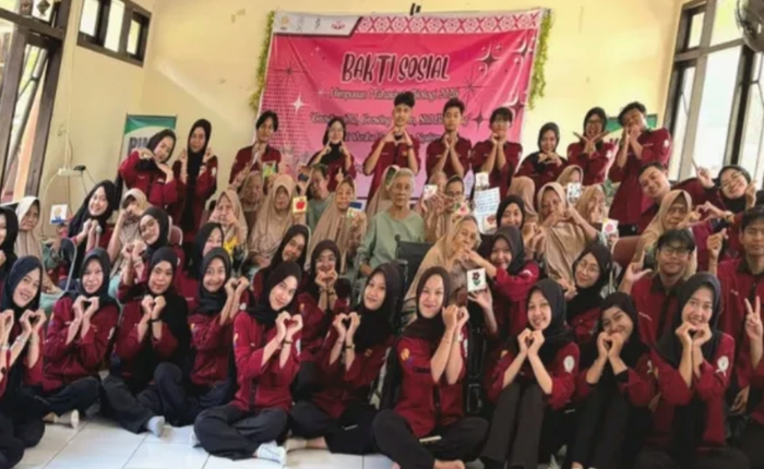 Puluhan mahasiswa pengurus Himabio FMIPA UNNES mengenakan kemeja korsa merah marun berpose membentuk simbol hati dengan tangan bersama warga lansia di depan spanduk bertuliskan Bakti Sosial Himpunan Mahasiswa Biologi.
