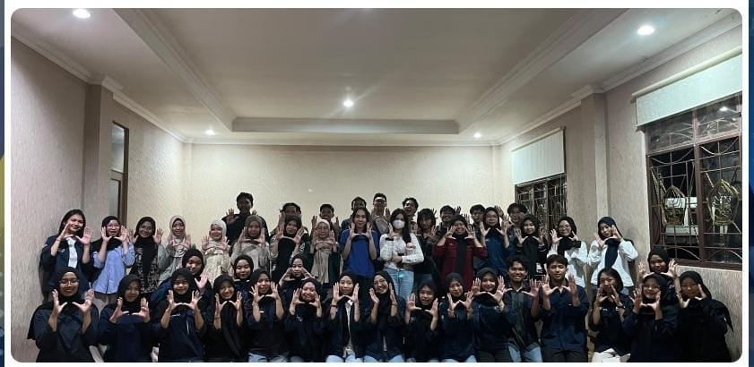 Puluhan mahasiswa pengurus BEM FMIPA UNNES berpose bersama dalam tiga barisan di dalam ruangan sambil kompak membentuk gestur tangan di depan dada.