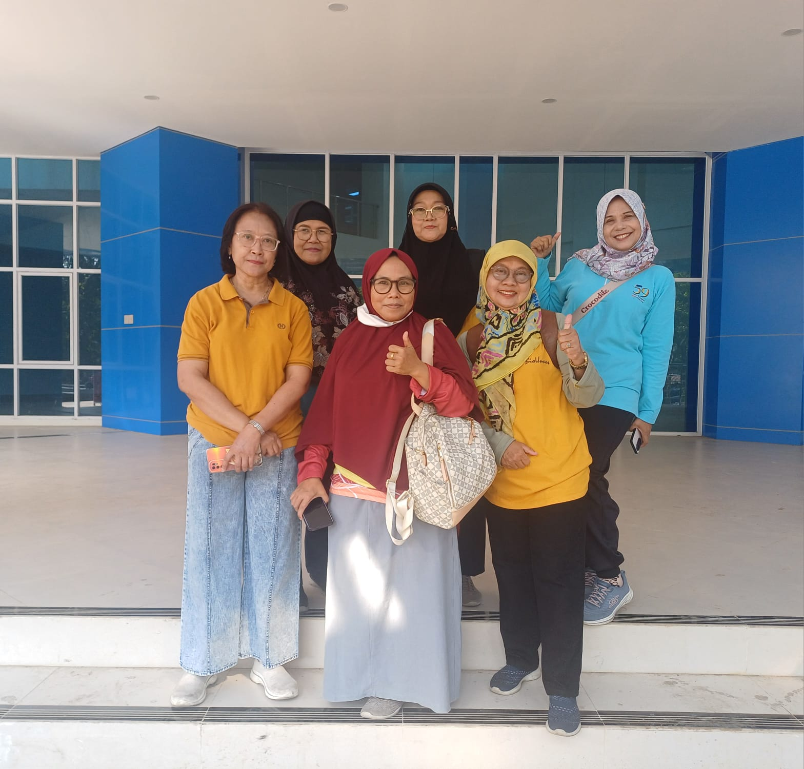 Six female professors and lecturers from the Biology Study Program at FMIPA UNNES standing together for a photo while smiling and giving a thumbs-up in front of a building with blue pillars.